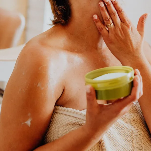 Mano aplicando crema en el cuello, con el tarro en la otra mano